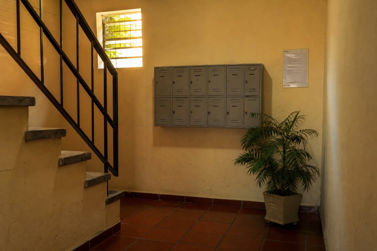 Hall de escada de um prédio pequeno de três andares com caixas de correio e um papel colado na parede