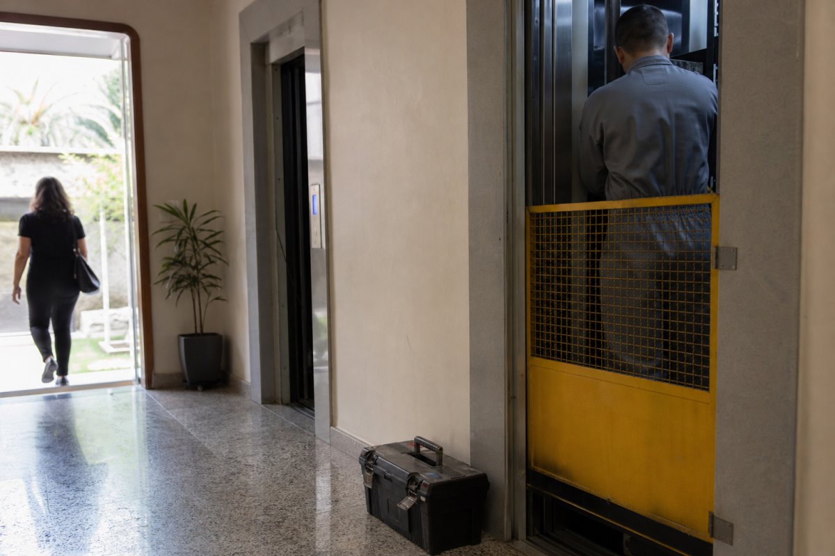 Técnico de costas fazendo manutenção no elevador do hall de um prédio residencial